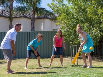 Man, woman, girl and boy playing cricket in backyard