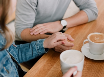 Man and woman holding hands with coffee on table