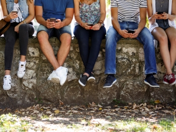 Young people sitting on wall looking at phones